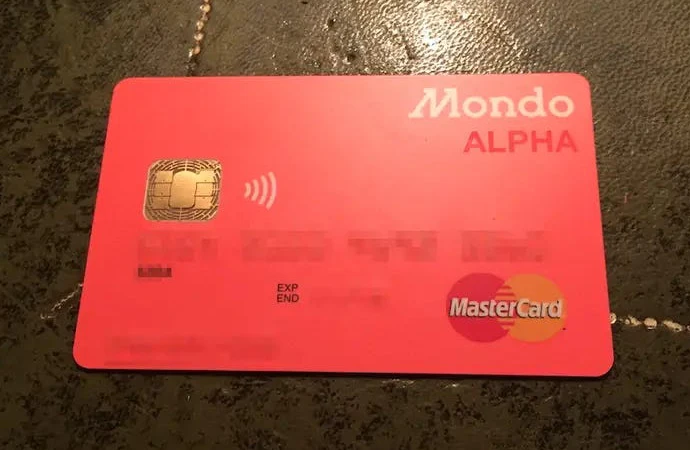 A bright coral prepaid card stamped with the word Alpha and the brand name Mondo, the original name of the UK challenger bank Monzo